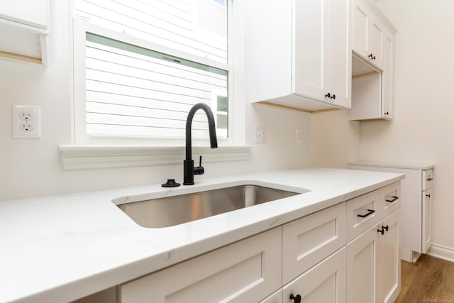 kitchen with light stone counters, light wood-type flooring, white cabinetry, and a sink