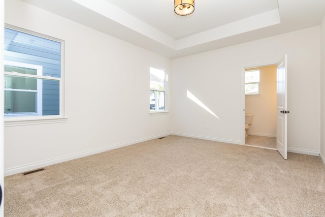 unfurnished room with carpet floors, a tray ceiling, visible vents, and baseboards