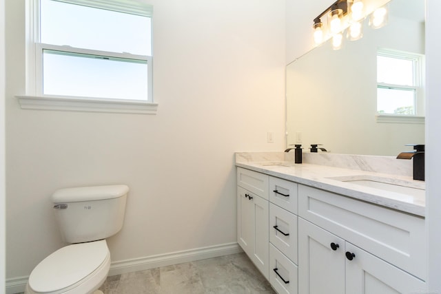 bathroom featuring double vanity, baseboards, toilet, and a sink