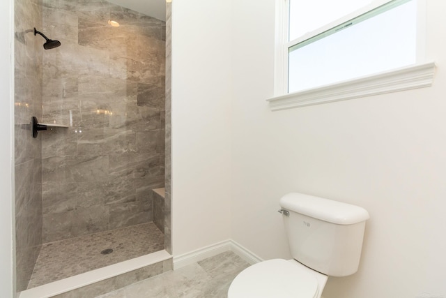 bathroom with toilet, baseboards, and tiled shower