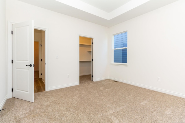 unfurnished bedroom featuring a walk in closet, a tray ceiling, a closet, carpet flooring, and baseboards