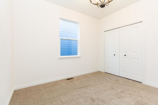 unfurnished bedroom featuring baseboards, visible vents, an inviting chandelier, carpet floors, and a closet