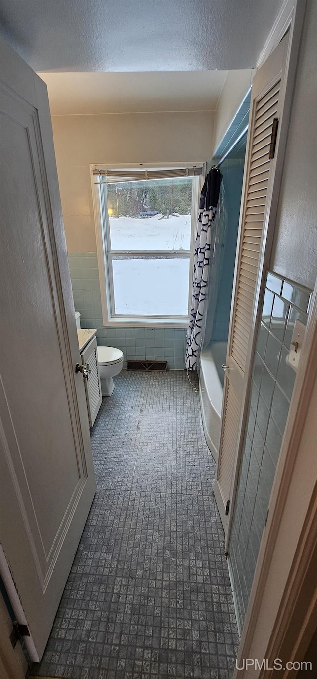 bathroom with shower / bath combo, tile walls, toilet, and a textured ceiling