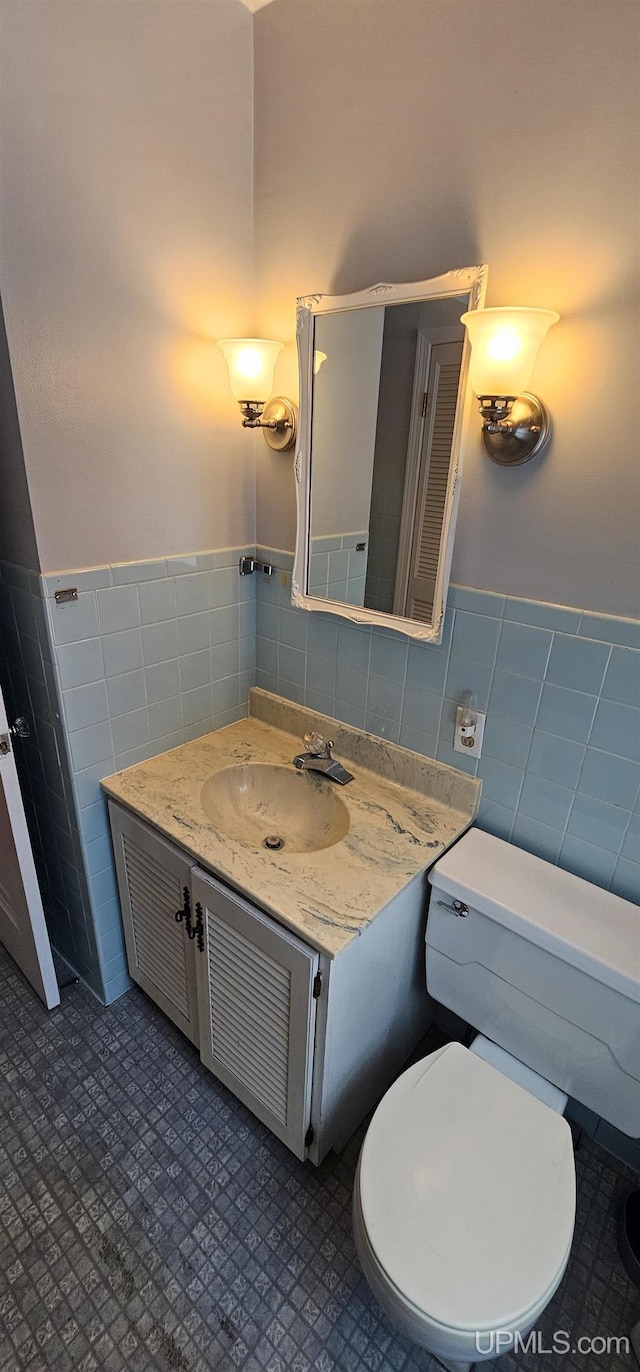 bathroom featuring a wainscoted wall, tile walls, toilet, and vanity