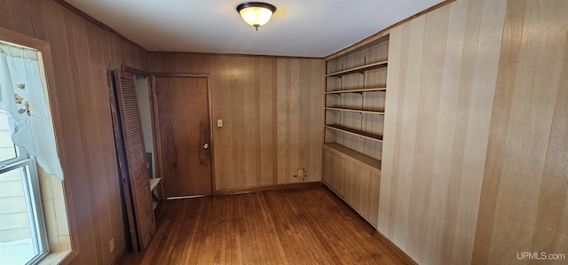 corridor with built in shelves, dark wood finished floors, and wooden walls