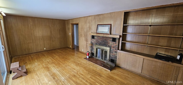 unfurnished living room featuring light wood-style floors, a fireplace, wooden walls, and baseboards