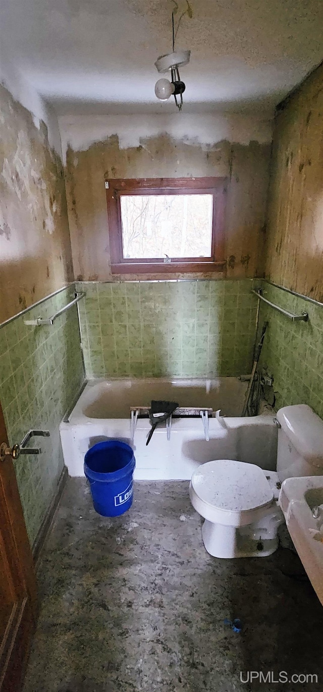 full bath featuring toilet, a tub, tile walls, and a wainscoted wall