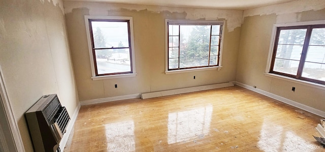 spare room featuring a baseboard heating unit, a wealth of natural light, light wood-type flooring, and heating unit