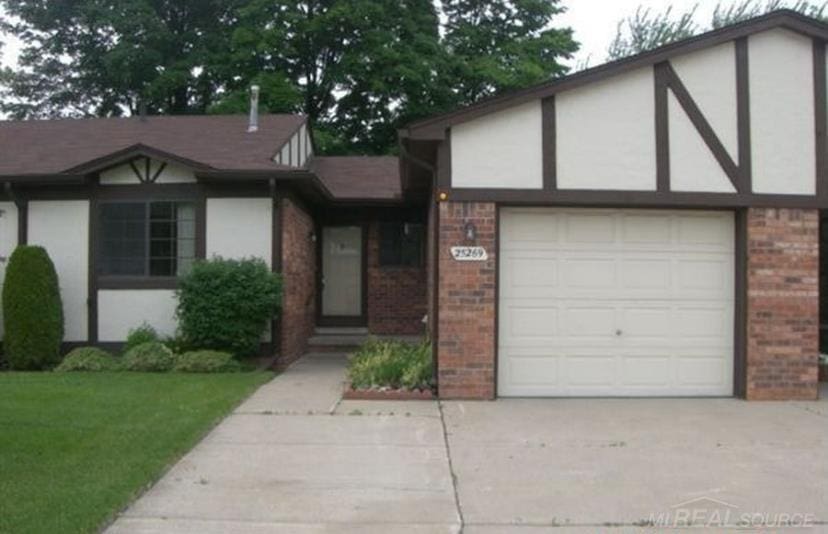 tudor-style house featuring brick siding, stucco siding, concrete driveway, an attached garage, and a front yard