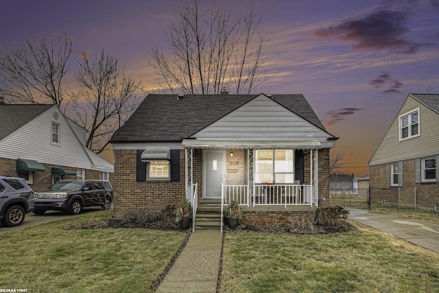 bungalow-style home featuring a yard, a porch, fence, and brick siding