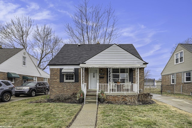 bungalow with a shingled roof, a front lawn, a porch, and brick siding