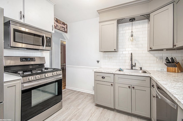 kitchen with a sink, light countertops, appliances with stainless steel finishes, wainscoting, and gray cabinets