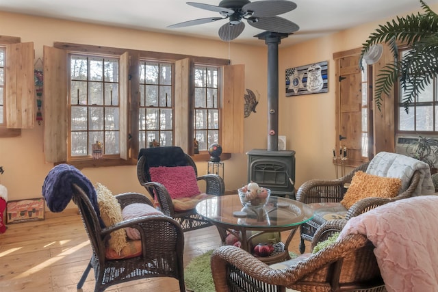 living area with ceiling fan, wood-type flooring, and a wood stove