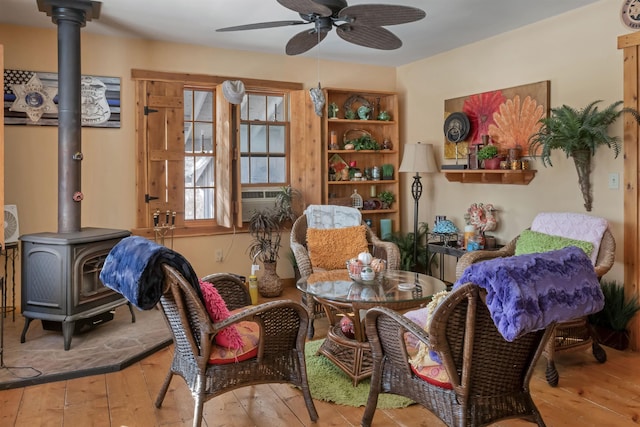 living area featuring a wood stove, cooling unit, a ceiling fan, and hardwood / wood-style floors