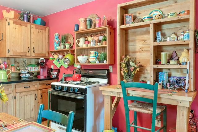 kitchen featuring open shelves, dark countertops, range with gas stovetop, and light brown cabinetry