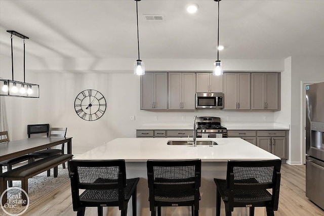 kitchen with light wood finished floors, appliances with stainless steel finishes, gray cabinets, light countertops, and a sink