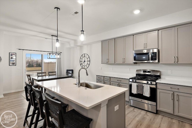 kitchen featuring gray cabinets, stainless steel appliances, light countertops, light wood-type flooring, and a sink