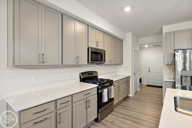 kitchen with stainless steel appliances, light wood finished floors, and gray cabinetry