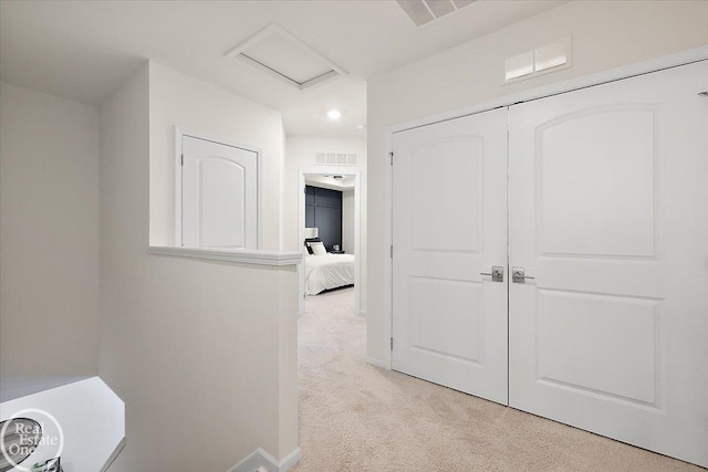 corridor featuring light carpet, attic access, visible vents, and baseboards