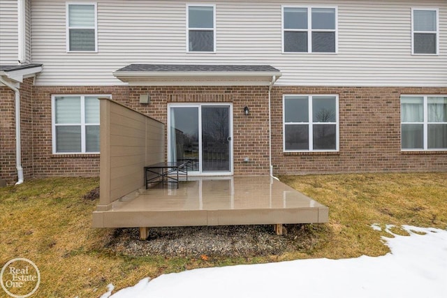 back of house with a yard, a shingled roof, a deck, and brick siding