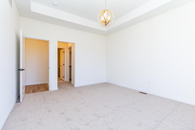 unfurnished room with a chandelier, a tray ceiling, light carpet, and baseboards