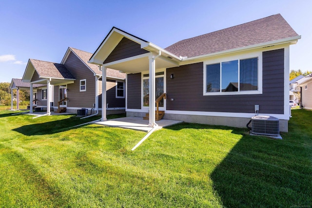 back of property with central air condition unit, a shingled roof, and a lawn