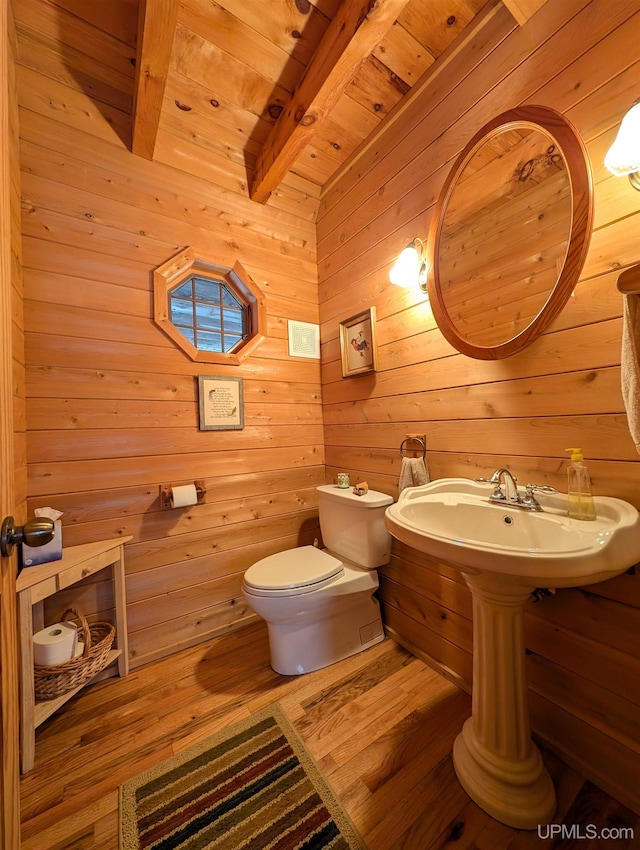 bathroom with beam ceiling, toilet, wooden walls, wood finished floors, and wooden ceiling