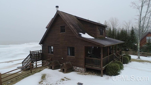 snow covered rear of property with covered porch, faux log siding, and roof with shingles