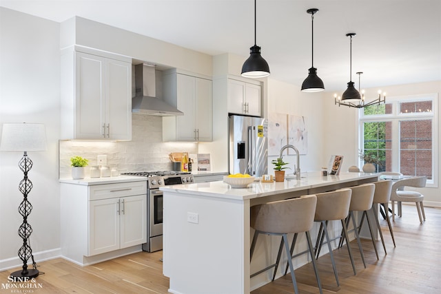 kitchen featuring tasteful backsplash, wall chimney exhaust hood, appliances with stainless steel finishes, a breakfast bar area, and light wood-style floors