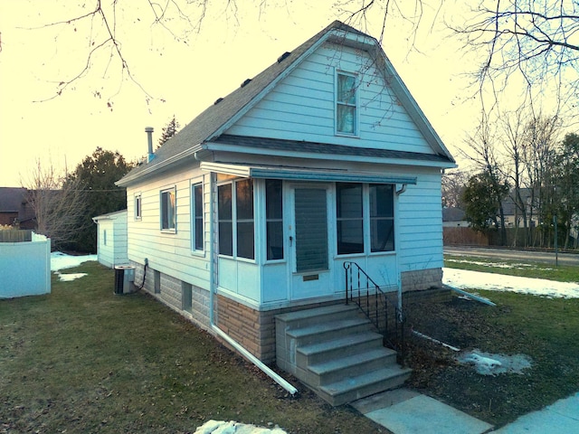 view of front facade featuring entry steps, roof with shingles, central AC unit, and a front lawn