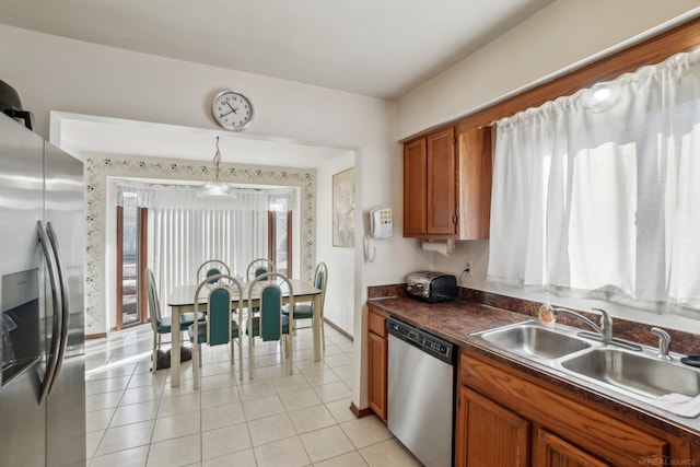 kitchen with brown cabinets, light tile patterned floors, dark countertops, appliances with stainless steel finishes, and a sink