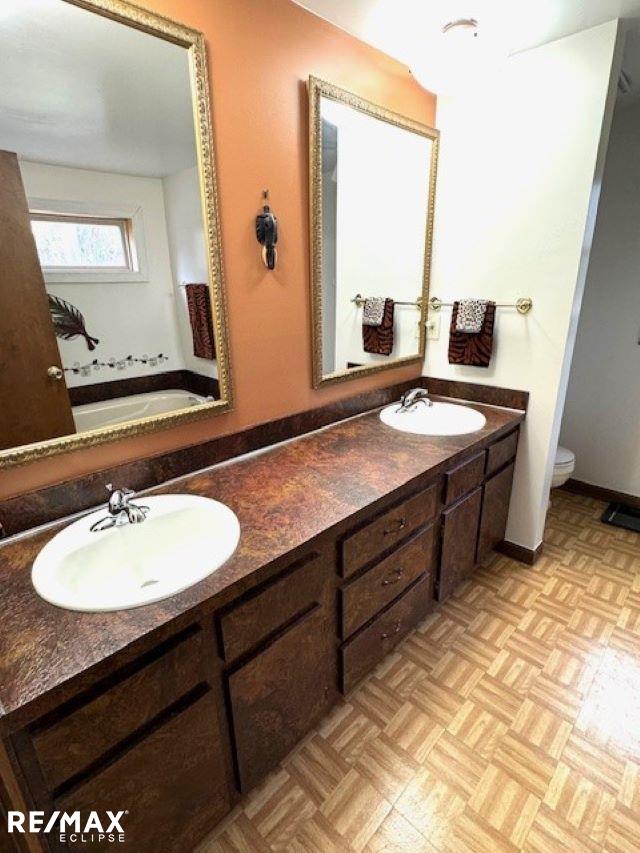 bathroom with baseboards, a sink, toilet, and double vanity