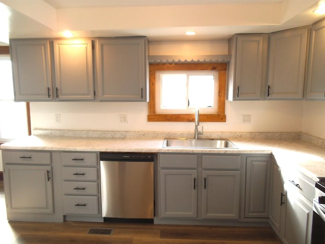 kitchen featuring dark wood-style floors, gray cabinets, light countertops, stainless steel dishwasher, and a sink