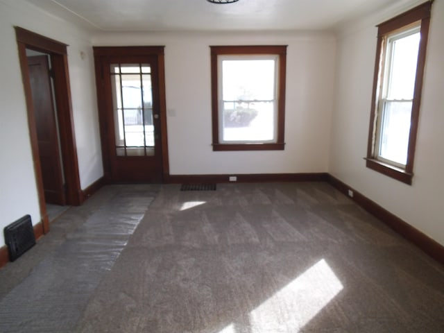 carpeted empty room featuring visible vents, baseboards, and a wealth of natural light