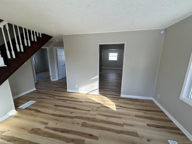 unfurnished room with a textured ceiling, wood finished floors, visible vents, baseboards, and stairway