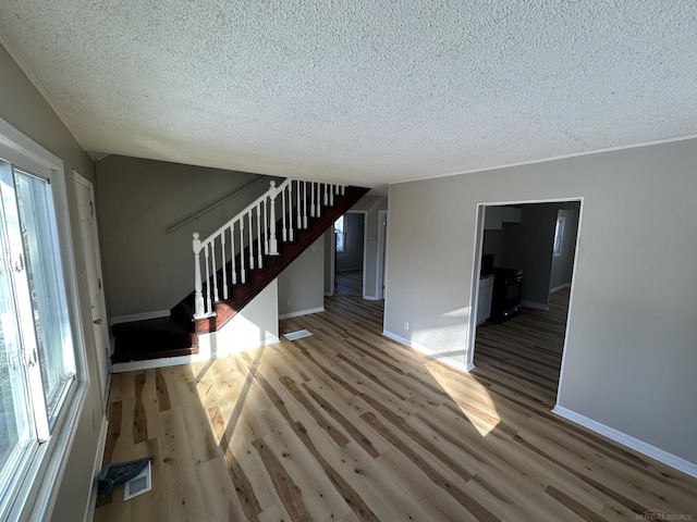 unfurnished living room featuring baseboards, a textured ceiling, stairway, and wood finished floors