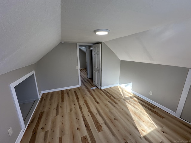 bonus room featuring lofted ceiling, light wood-style flooring, baseboards, and a textured ceiling