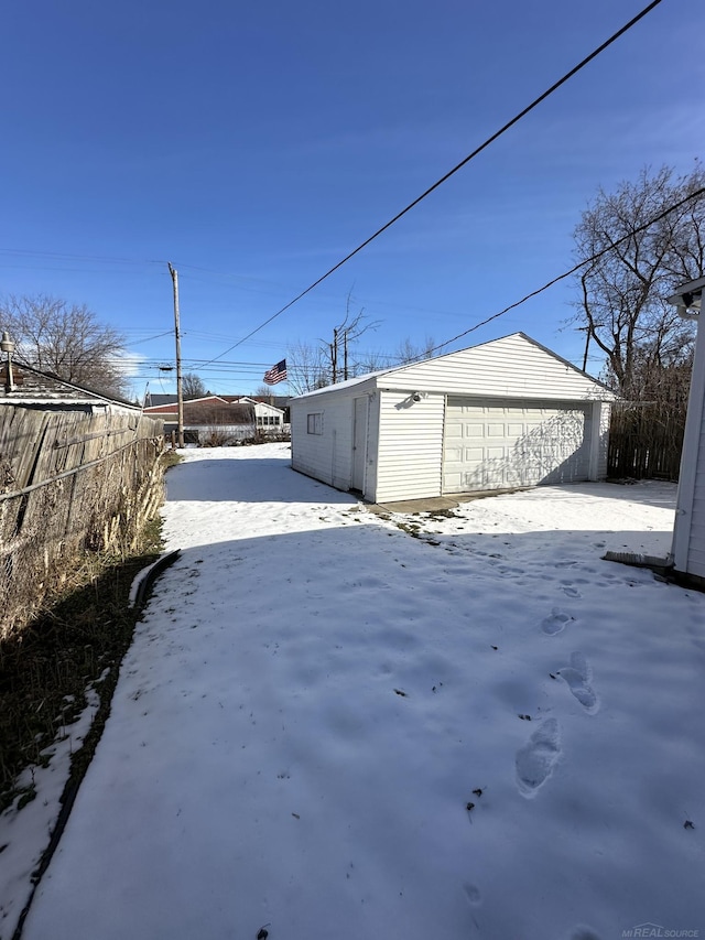 snowy yard featuring an outbuilding, a detached garage, and fence