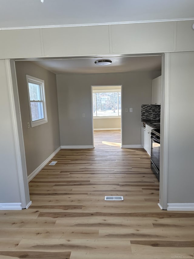 interior space featuring decorative backsplash, gas stove, white cabinetry, light wood-type flooring, and plenty of natural light