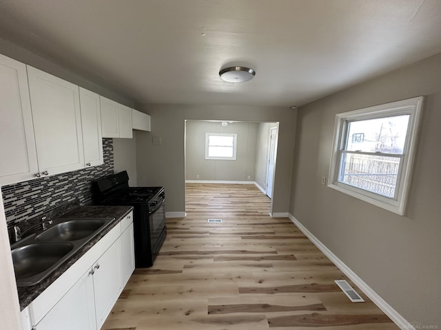 kitchen with a sink, visible vents, black gas stove, backsplash, and dark countertops