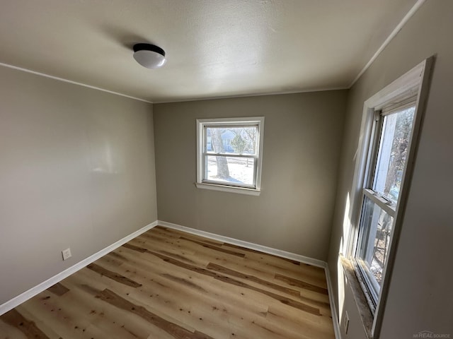 spare room with ornamental molding, light wood-type flooring, and baseboards