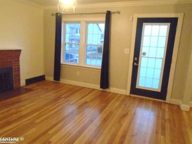 unfurnished living room with ornamental molding, a brick fireplace, baseboards, and wood finished floors