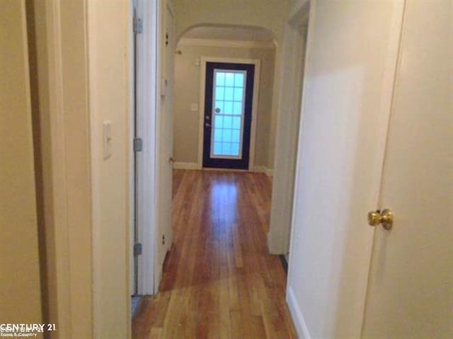 hall featuring crown molding, baseboards, arched walkways, and wood finished floors