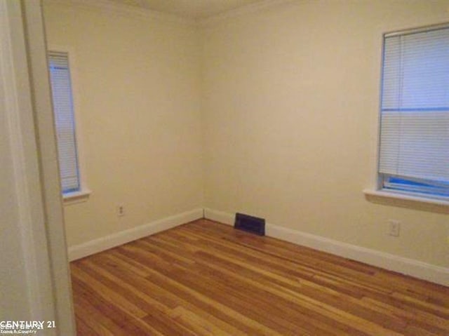 empty room with baseboards, visible vents, wood finished floors, and ornamental molding