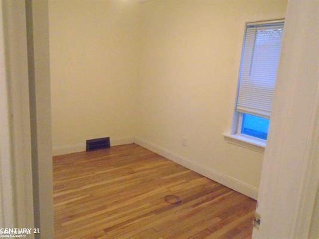 empty room with baseboards, visible vents, and wood finished floors