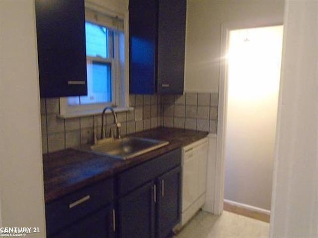 kitchen featuring tasteful backsplash, dark countertops, a sink, dishwasher, and baseboards