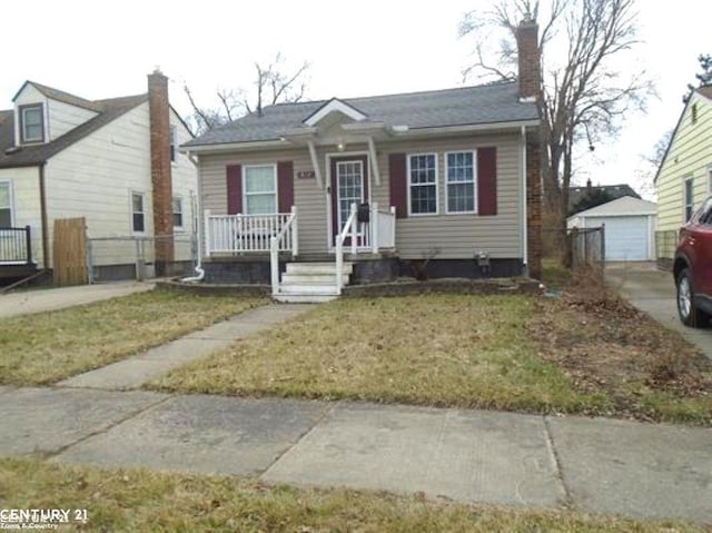 bungalow featuring concrete driveway, a detached garage, an outbuilding, covered porch, and a front lawn