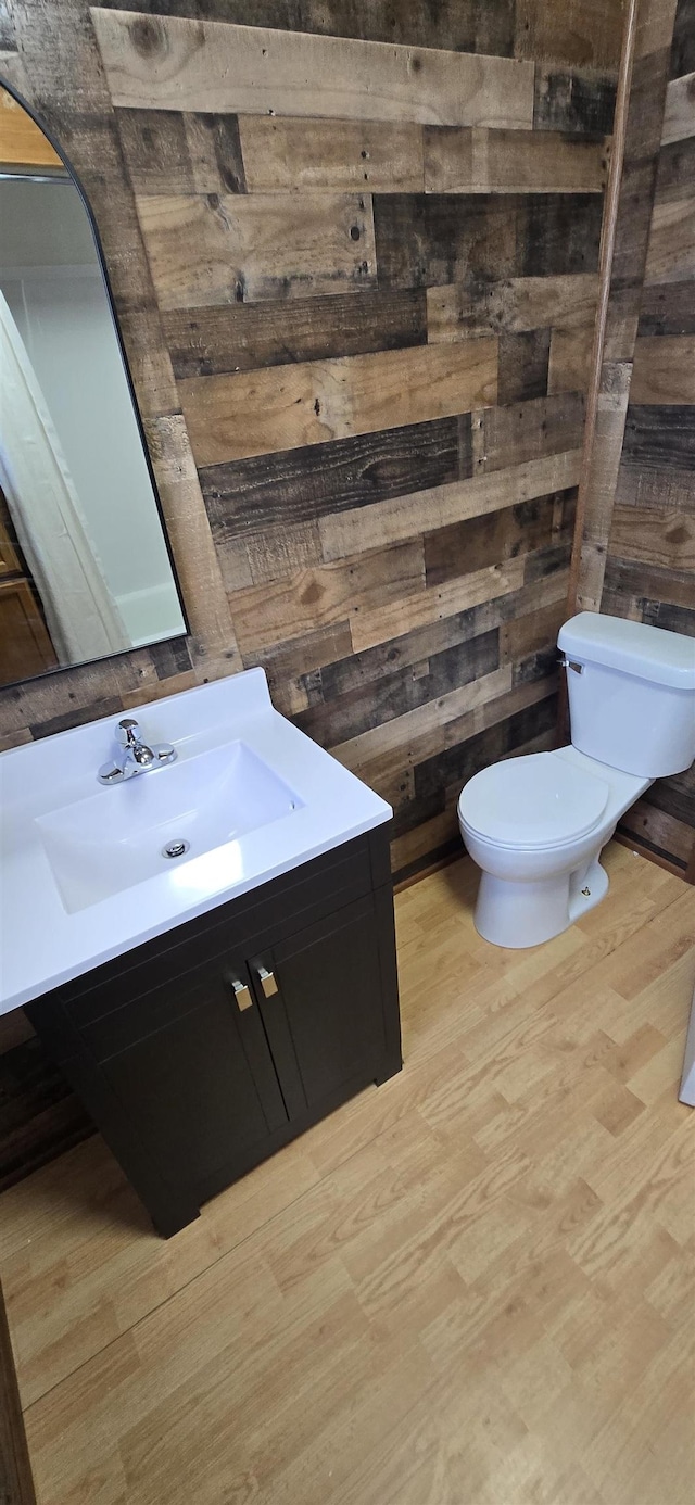 half bath with toilet, wooden walls, wood finished floors, and vanity