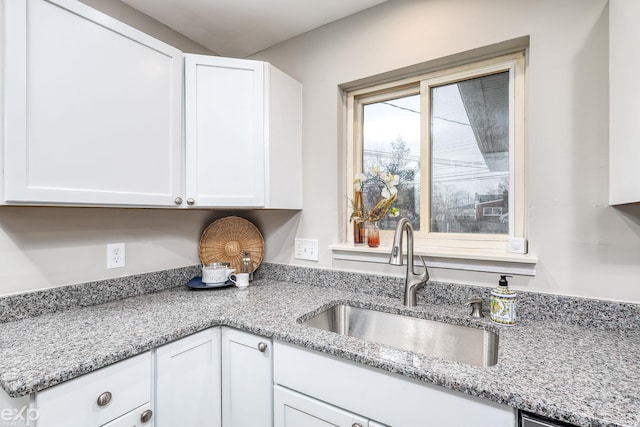 kitchen featuring light stone countertops, white cabinetry, and a sink