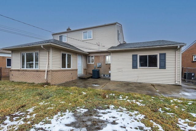 snow covered property featuring central AC, brick siding, fence, a yard, and a patio area